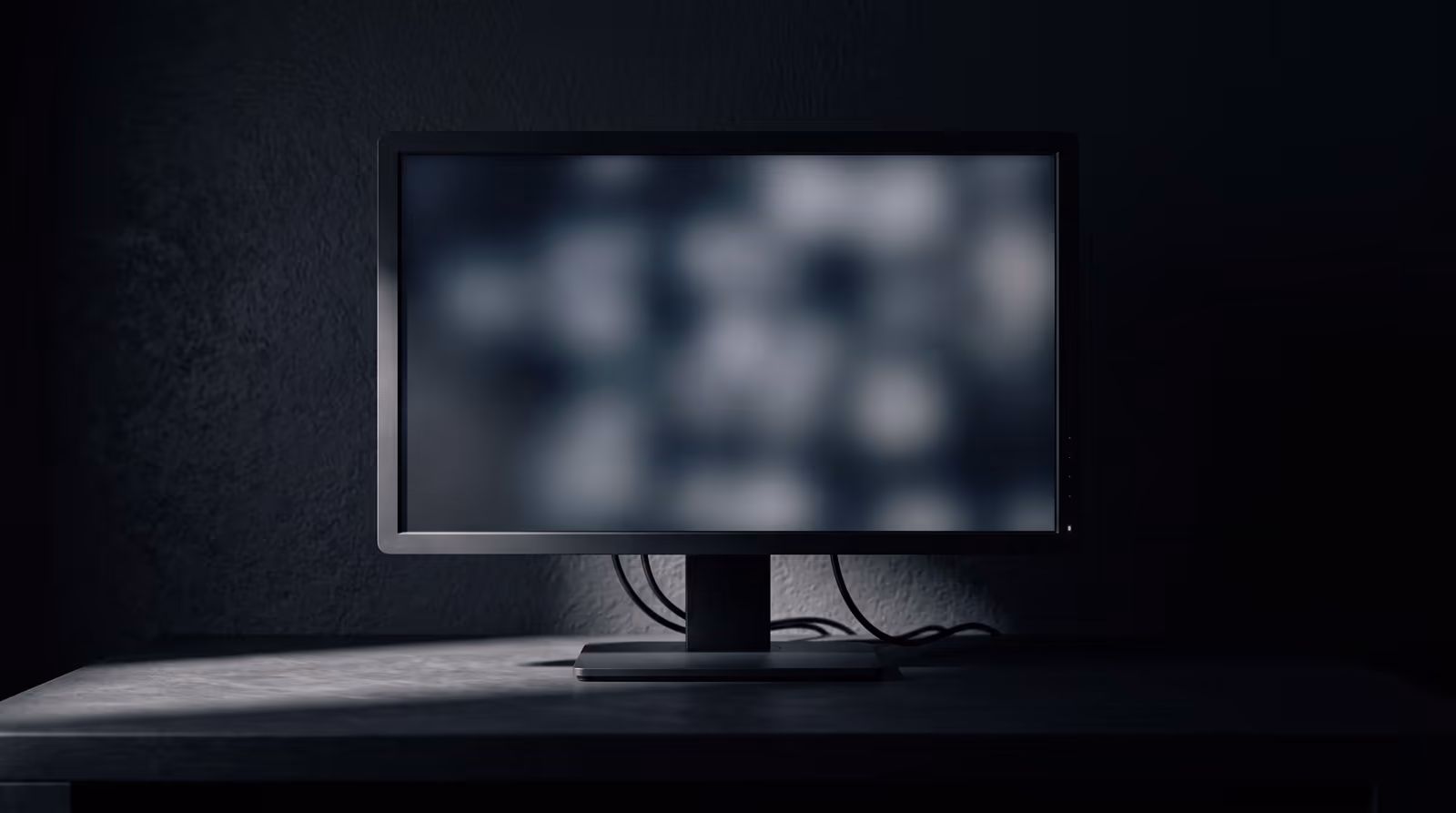 A monitor and keyboard on a desk, lit by a single lamp in a dark room