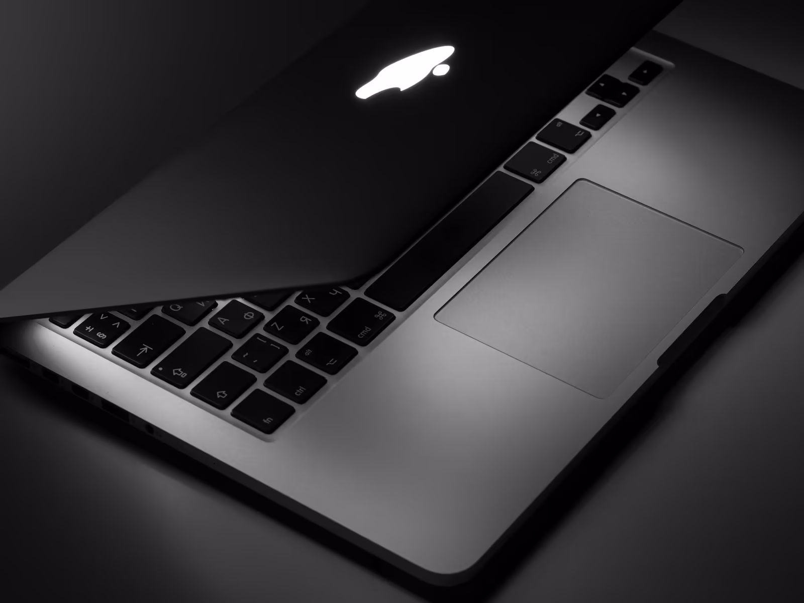 A MacBook half open in the dark, its logo lit
